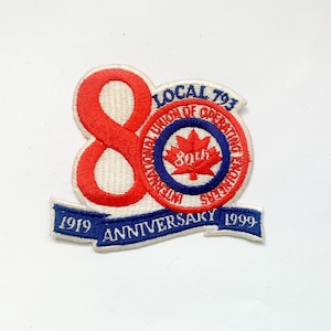 Może przedstawiać: Haftowana naszywka upamiętniająca 80. rocznicę powstania International Union of Operating Engineers Local 793. Zawiera dużą czerwoną cyfrę "80" oraz okrągły emblemat z liściem klonu. Na bannerze widnieje napis "1919 Anniversary 1999".