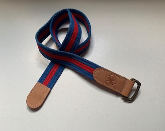 May include: A blue and red striped canvas belt with a brown leather buckle featuring a four-leaf clover design.
