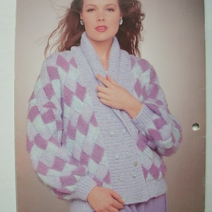 Peut inclure: Un cardigan de couleur lilas clair avec un motif en losanges. Le cardigan a un col ch&acirc;le et une fermeture &agrave; boutons. Le mannequin porte une jupe lilas clair assortie.