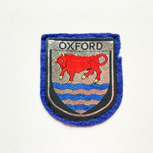 May include: A blue felt patch with a silver shield featuring a red bull and the word "OXFORD" in white.