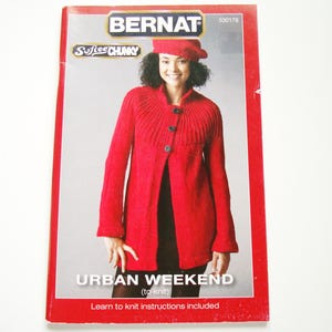 Pode incluir: Um livreto de padrões de tricô Bernat Softee Chunky intitulado Urban Weekend. A capa apresenta um cardigã vermelho brilhante de manga comprida com um jugo canelado e três botões escuros. O texto inclui Bernat, Softee Chunky, 530178 e Learn to knit instructions included.