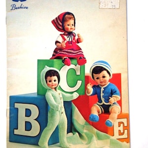 Puede incluir: Un libro vintage de patrones de tejido para muñecas, titulado "Just for Dolls" con un logotipo de colmena y las palabras "Patons Beehive" en la portada. El libro presenta tres muñecas vestidas con atuendos tejidos, sentadas en bloques que deletrean "BCE".