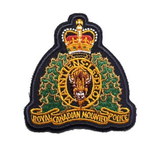 Peut inclure: Un écusson brodé représentant l'emblème de la Gendarmerie royale du Canada. Le motif comprend une tête de bison centrale, une couronne au sommet, des feuilles d'érable vertes et une bannière dorée avec le texte ROYAL CANADIAN MOUNTED POLICE.