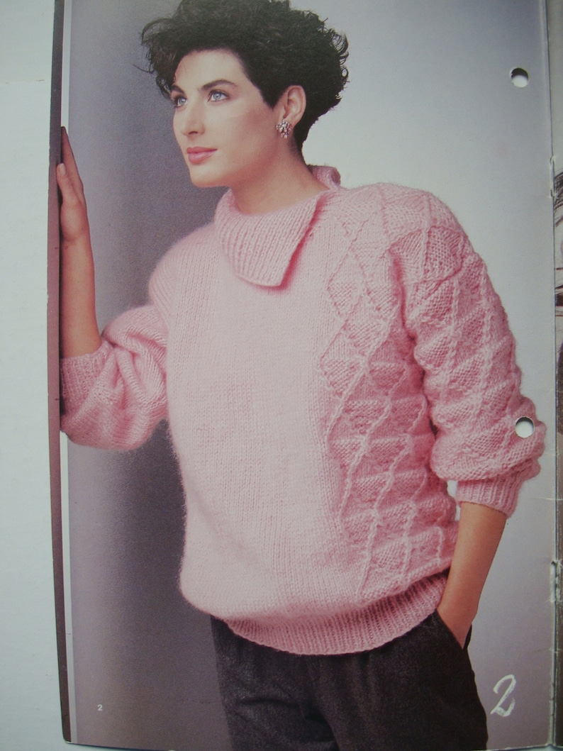 Peut inclure: Un pull rose en tricot avec un motif de tricot torsad&eacute; sur les manches et un col. Le pull est port&eacute; par une personne aux cheveux courts et fonc&eacute;s.