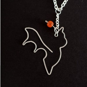 May include: A silver necklace with a wire bat pendant and an orange bead. The bat is flying with its wings spread out.