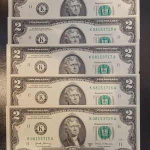 Pode incluir: Cinco notas de dois dólares com o retrato de Thomas Jefferson. As notas são todas da mesma série e têm o mesmo prefixo de número de série, K08153715A. As notas estão em bom estado e não têm rasgos ou dobras visíveis.