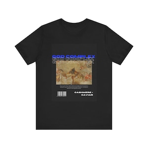 May include: Black t-shirt with a graphic print of a painting of angels in the clouds. The text "GOD COMPLEX" is repeated three times in blue and the text "CASHMERE + CAVIAR" is printed below the image.
