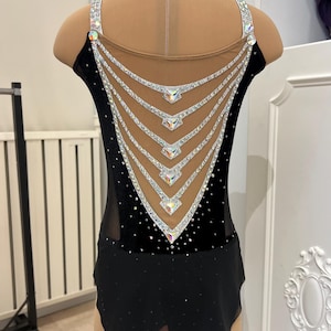 May include: Black velvet figure skating dress with a sheer mesh back and a crystal design. The back features a V-shaped design with multiple rows of crystals.