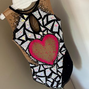 May include: A sleeveless leotard featuring a black and nude mesh base with a central hot pink heart motif. The garment is heavily embellished with geometric white and iridescent crystal shards, along with scattered small dark and clear rhinestones.