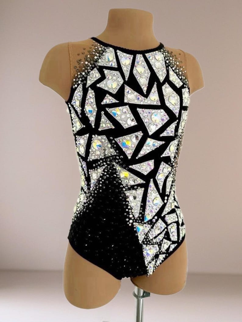 May include: A sleeveless leotard featuring a black base with a geometric pattern of white triangular shapes. The garment is heavily embellished with iridescent crystals and rhinestones, with sheer nude mesh fabric at the upper chest and shoulders.