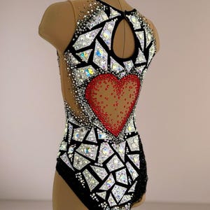 May include: A sleeveless leotard featuring a black base with a large red heart motif on the back. The garment is decorated with numerous clear and iridescent crystals arranged in geometric, mosaic-like patterns across the bodice and neckline.