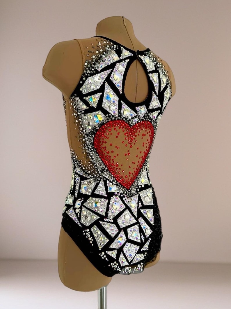 May include: A sleeveless leotard featuring a black base with a large red heart motif on the back. The garment is decorated with numerous clear and iridescent crystals arranged in geometric, mosaic-like patterns across the bodice and neckline.