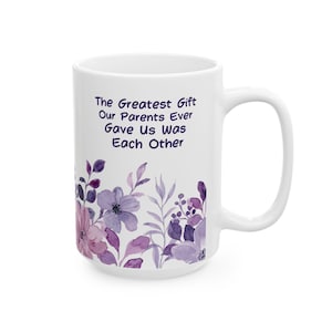 May include: White ceramic mug with a purple floral design and the text "The Greatest Gift Our Parents Ever Gave Us Was Each Other".