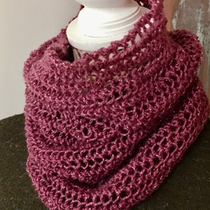 May include: A mauve crocheted cowl with a delicate openwork pattern. The cowl is made with a sparkly yarn and is displayed on a white mannequin.
