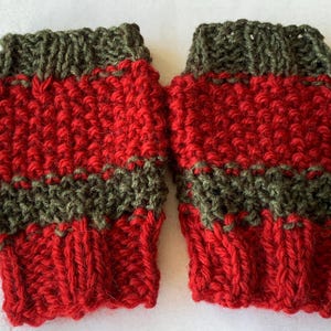 May include: A pair of knitted fingerless gloves. The gloves are predominantly red with olive green bands at the cuff and mid-section. The knitted texture is visible, highlighting the handmade quality of the item.