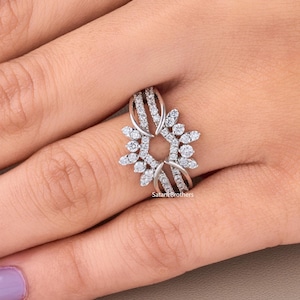 May include: A silver ring with a floral design, set with multiple small, clear gemstones. The ring features a central open circle surrounded by a pattern of curved lines and smaller gemstones. The ring is on a hand with purple nail polish.