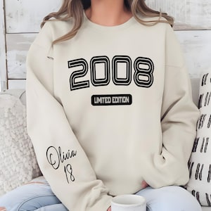 May include: Cream-colored sweatshirt with the year "2008" in bold black outlined font, and the words "LIMITED EDITION" below. The sleeve features the name "Olivia" and the number "18" in a cursive font.