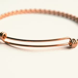 May include: A rose gold expandable bangle bracelet with a braided design.