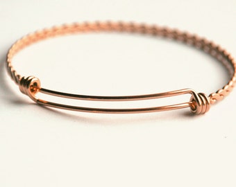 May include: A rose gold expandable bangle bracelet with a braided design.