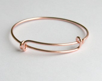 May include: A rose gold adjustable bangle bracelet. The bracelet features a simple, elegant design with a circular band and a sliding mechanism for size adjustment. The metal has a warm, metallic sheen.