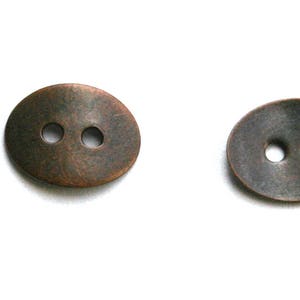 May include: Two oval-shaped copper buttons with two holes each. The buttons have a slightly textured surface.