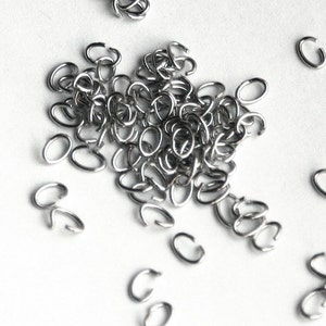 May include: A pile of silver jump rings, a type of jewelry finding, scattered on a white surface.