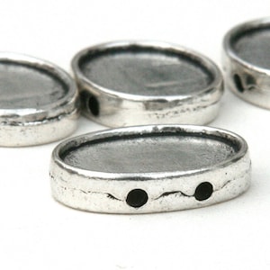 May include: Four silver oval-shaped metal beads with a smooth, slightly textured surface. Each bead has two holes for stringing.