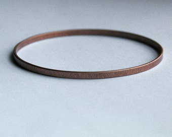 May include: A simple, thin, copper bangle bracelet. The bracelet is smooth and has a slightly hammered texture.