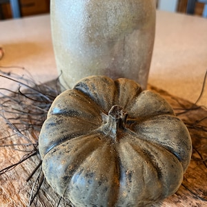 Peut inclure: Une petite citrouille en céramique de couleur brun foncé avec une surface texturée. La citrouille est posée sur un morceau de bois de couleur brun et noir.