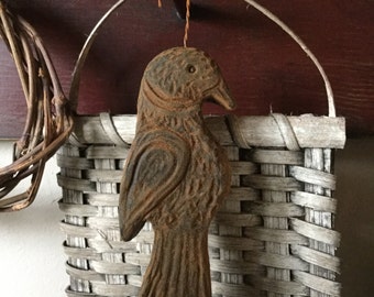 May include: A rustic brown bird ornament with a carved design, hanging from a woven basket with a whitewashed finish.