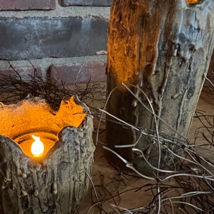 May include: Two brown ceramic candle holders with a textured, tree bark-like design. The candle holders are lit with warm, yellow candlelight. The candle holders are sitting on a bed of brown twigs.