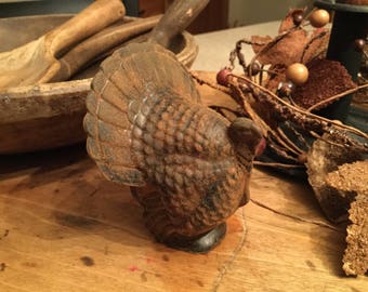 May include: A rustic brown and black cast iron turkey figurine with a detailed feathered design. The figurine is sitting on a wooden surface.