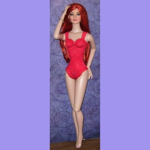 May include: A red lace bodysuit with a sweetheart neckline. The doll has long, red hair and is wearing a gold bracelet.