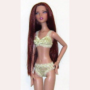 May include: A fashion doll with long auburn hair and blue eyes, wearing a light green lace bra and matching underwear. The doll has a slender build and is posed against a plain white background.