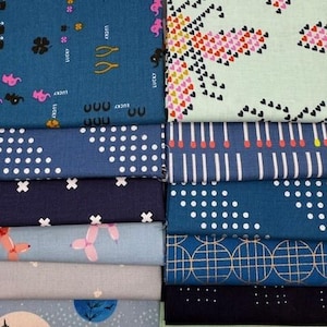 May include: A stack of patterned fabric in various shades of blue, gray, and green. Designs include polka dots, crosses, balloons, and geometric shapes. Some fabrics have the word "LUCKY" printed on them.