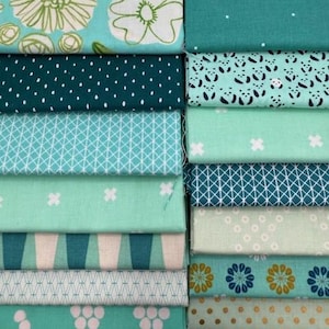 May include: A stack of various teal and green fabric swatches. The fabrics feature floral, geometric, and dotted patterns. Some fabrics have white or gold accents. The fabrics are neatly folded and stacked, showcasing a variety of designs and textures.