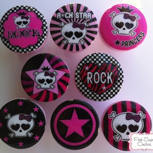 May include: Eight round pink, black, and white buttons with skull and star designs. The buttons have the words "Rock", "Rock Star", "Princess", and "Pink Sugar Couture".