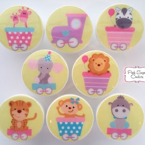 Könnte beinhalten: Eine Sammlung von acht runden Schrankknöpfen mit Cartoon-Tierdesigns. Jeder Knopf zeigt ein anderes Tier, darunter eine Giraffe, ein Zebra, ein Elefant, ein Löwe, ein Tiger, ein Affe und ein Nilpferd, die in einem Zugwagen fahren. Die Knöpfe haben einen gelben Hintergrund.