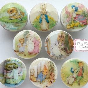 Puede incluir: Conjunto de 8 pomos redondos de cerámica con ilustraciones de los libros infantiles de Beatrix Potter. Los pomos presentan personajes como Peter Rabbit, Jemima Puddle-Duck y Mrs. Tiggy-Winkle.