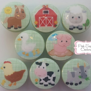 Puede incluir: Conjunto de ocho pomos redondos, verdes y blancos con ilustraciones de animales de granja. Los animales incluyen un caballo, un cerdo, una vaca, un pato, una gallina, una oveja y dos terneros. Los pomos están decorados con un patrón de cuadros verdes y blancos.