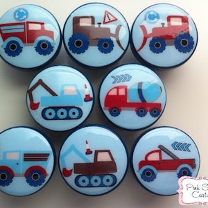 May include: Set of 8 blue and white round knobs with different construction vehicle designs. The knobs feature red, brown, and blue vehicles with black wheels. The knobs are perfect for adding a fun and whimsical touch to any room.