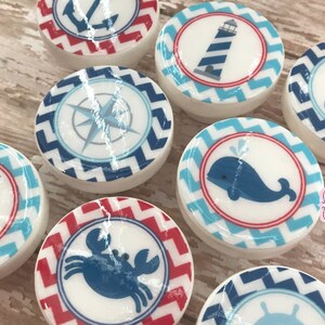 May include: Set of 8 nautical themed round ceramic drawer knobs with red and blue chevron patterns. Each knob features a different nautical image: anchor, lighthouse, compass, sailboat, whale, crab, and two others.
