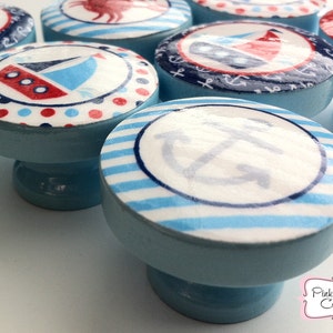 May include: Set of six blue and white nautical themed cabinet knobs with various designs including a sailboat, anchor, and stripes.