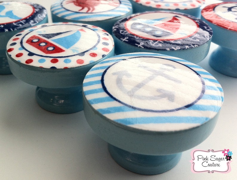 May include: Set of six blue and white nautical themed cabinet knobs with various designs including a sailboat, anchor, and stripes.