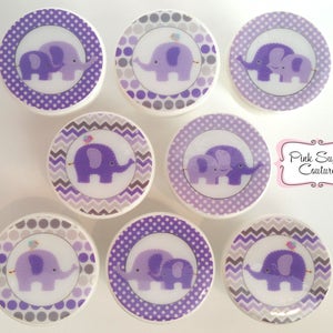 May include: Set of eight purple and gray round drawer knobs with a chevron, polka dot, and solid purple background. Each knob features a purple elephant with a small bird on top.