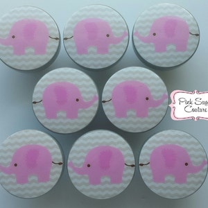 Peut inclure: Ensemble de huit boutons de tiroir en forme d'éléphant gris et rose avec un motif chevron. Les boutons mesurent environ 5 cm de diamètre.