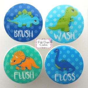 May include: Four round blue and green stickers with white polka dots and dinosaur illustrations. Each sticker has a different dinosaur and a word: "BRUSH", "WASH", "FLUSH", and "FLOSS".
