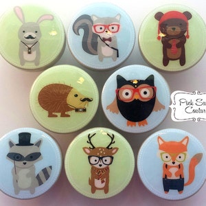 Op de afbeelding: Set van zeven ronde, kleurrijke, keramische knoppen met grillige dierillustraties. Elke knop heeft een ander dier dat een bril en een strikje draagt, waaronder een konijn, een eekhoorn, een beer, een egel, een uil, een hert en een vos. De knoppen zijn perfect om elke kamer een vleugje grilligheid te geven.