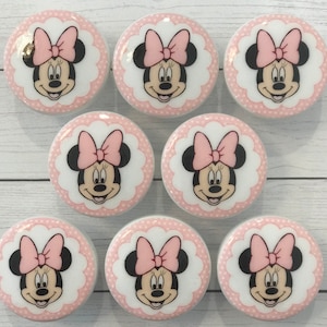 Può includere: Otto pomelli rotondi per cassetti in ceramica bianca con un motivo a pois rosa. Ogni pomello presenta un'immagine di cartone animato di Minnie Mouse con un fiocco rosa.