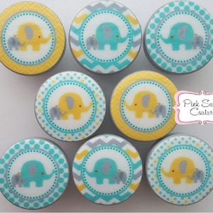 May include: Nine round, decorative, wooden knobs with a white background and a blue or yellow elephant design. The elephants are surrounded by a circle of dots or a chevron pattern. The knobs are perfect for adding a touch of whimsy to any room.